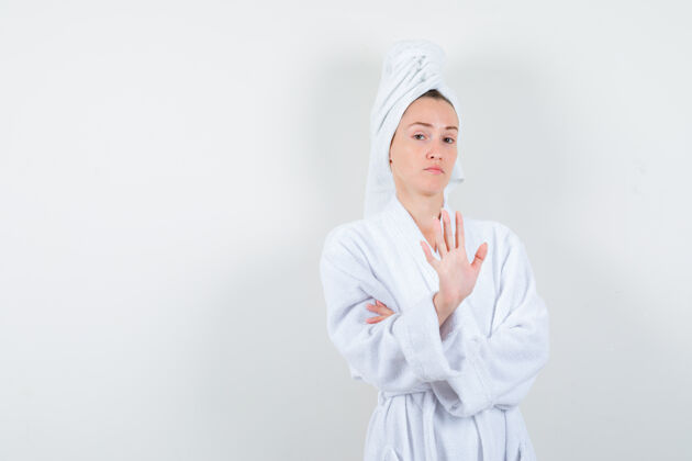 女孩在白色浴袍 毛巾和看起来自信的前视图显示停止手势的年轻女子的肖像一起毛巾年轻
