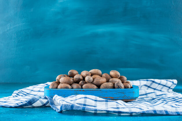 美味山核桃坚果放在一个木制盘子上 茶巾放在蓝色的表面上美味天然美味