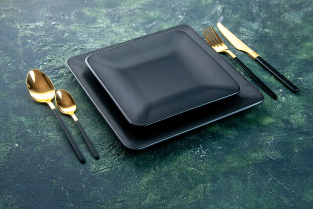 刀正面是黑色的方形盘子 黑色背景上有金色的叉子 勺子和小刀深色叉子食物