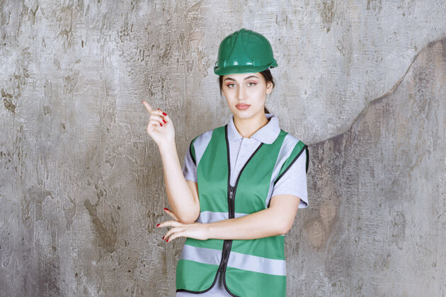 成人身着绿色制服 头戴头盔的女工程师 表情丰富地展示着左侧工人姿势标准