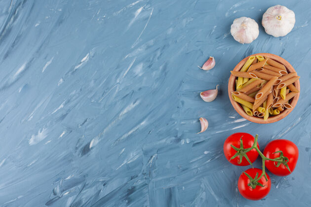 视图蓝色桌子上放着一碗五颜六色的生面食 里面有大蒜素和新鲜的红色西红柿多黄色颜色