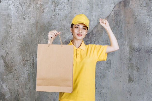 快递身着黄色制服的女服务人员手持购物袋 并显示积极的手势送货成人人