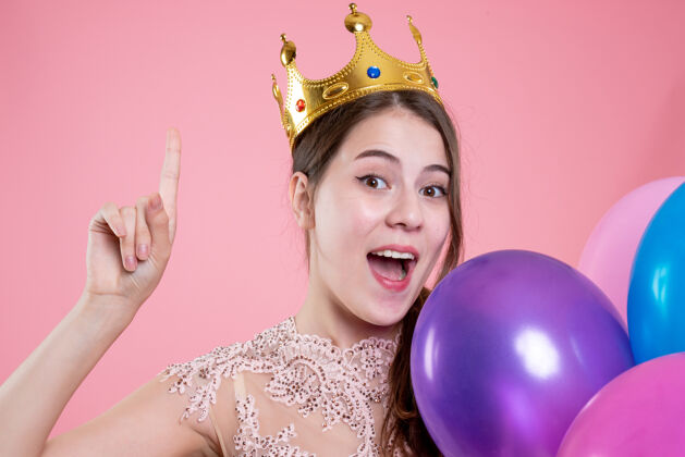 粉红色特写前视图可爱的聚会女孩与皇冠举行气球指着手指向上人贵族向上
