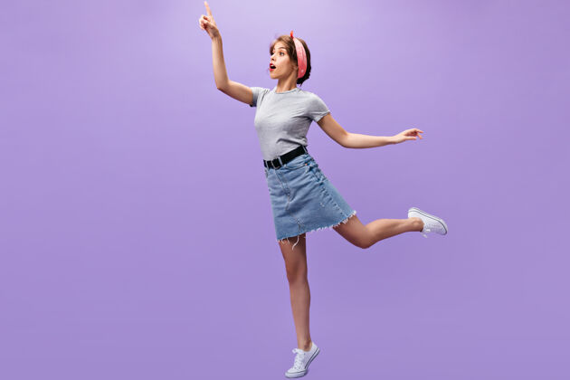 时尚穿着牛仔装的苗条女孩摆姿势紫色背景穿着白色运动鞋和时髦衬衫的粉色大手帕 让年轻女士大吃一惊紫色休闲头发