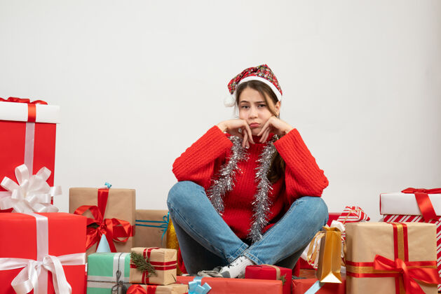 时尚前视图困惑的女孩和圣诞帽坐在周围的礼物购物节日圣诞老人