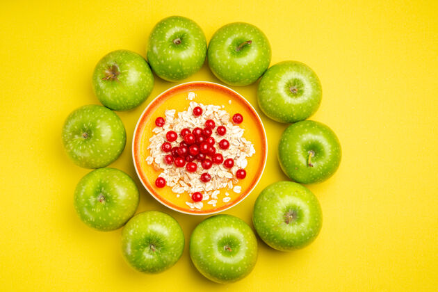 可食用水果从远处俯瞰苹果绿色苹果黄色桌子上一碗红醋栗燕麦片碗鳄梨葡萄干
