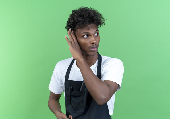 非裔美国人看着一边想着年轻的美国黑人男理发师穿着制服 在绿色背景上显示出一种孤立的倾听姿态理发师壁板男性