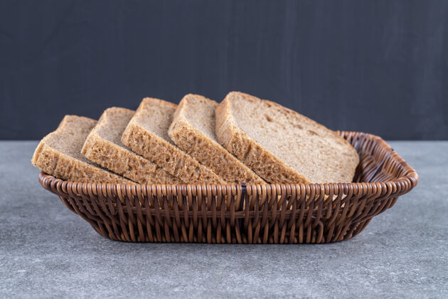 面包屑石桌上放着柳条筐的黑面包片食品吐司切