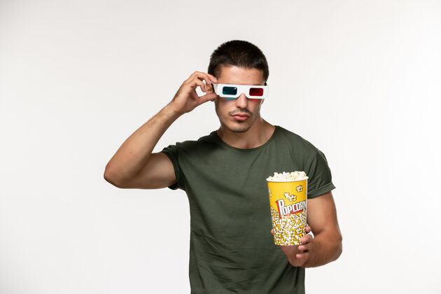 年轻的男人正面图身穿绿色t恤的年轻男性手持爆米花in-d太阳镜在白色办公桌上看电影孤独电影院男性电影爆米花肖像电影