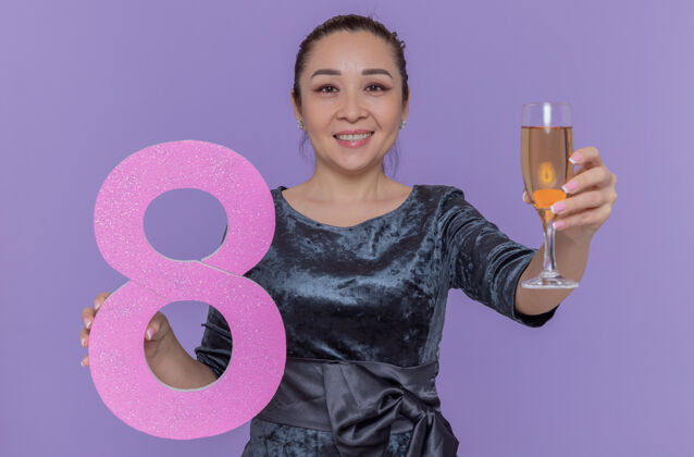香槟快乐的亚洲女人拿着用硬纸板和香槟制成的8号酒杯 站在紫色的墙上高高兴兴地笑着庆祝国际妇女节国际微笑女人