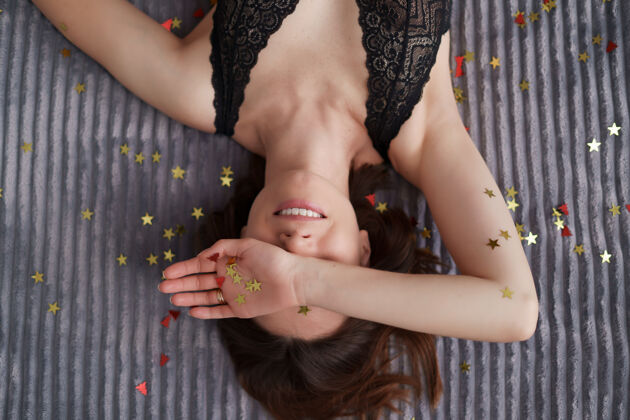 华丽微笑的女人躺在用金色五彩星星装饰的灰色软垫上谎言美女柔软