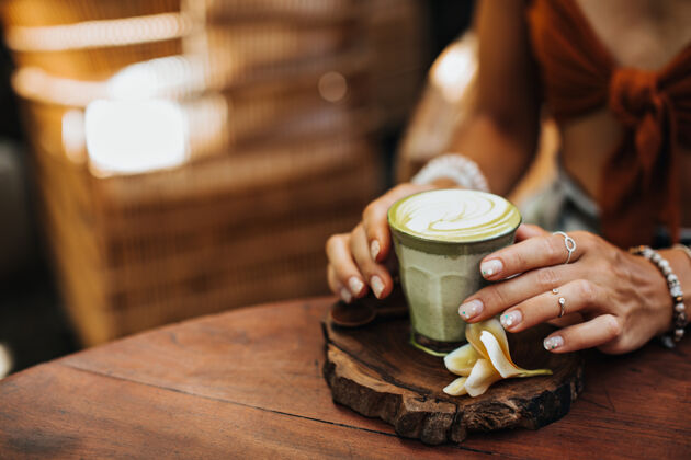 木头戴着银戒指的女性手拿着一杯抹茶拿铁茶热抹茶