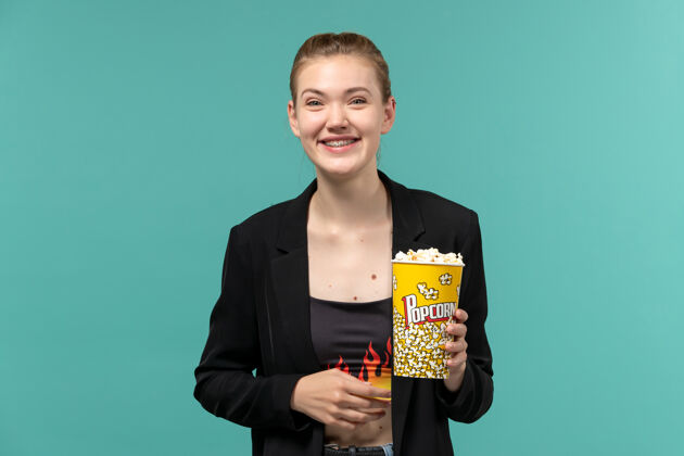 电影正面图：年轻女子拿着爆米花包 在蓝色的水面上看电影大笑电影电影院年轻的女性