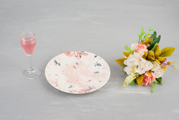 单身鲜花 盘子和一杯玫瑰红酒放在灰色的表面上花叶子盘子