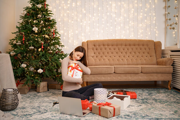 生动一个女人坐在装饰好的圣诞礼物盒中间拥抱着许多礼物庆祝积极愿望