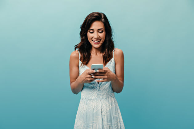 衬衫调皮的白裙女孩微笑着在蓝色背景的智能手机里聊天心情愉快的可爱女人拿着手机室内脸休闲