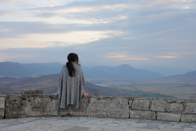 年轻一位年轻女子欣赏卡拉巴赫美丽山景的后视图高自然石头