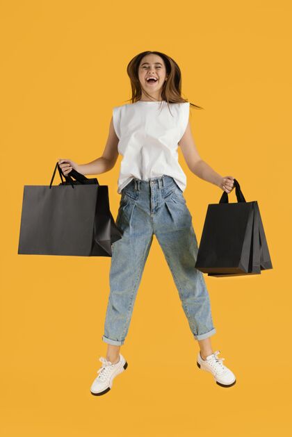 女人带着购物袋跳跃的年轻女性肖像模特美丽购物袋