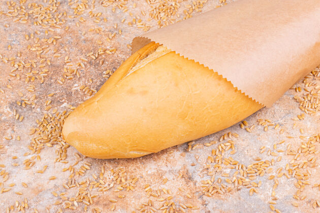 面粉面包在纸袋旁边撒上麦粒 放在大理石桌上营养面包营养