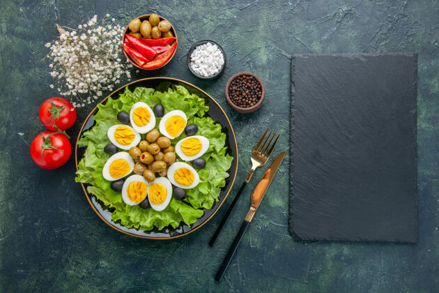 餐厅俯视图煮熟的鸡蛋片 绿色沙拉和橄榄 深蓝色背景沙拉茶餐