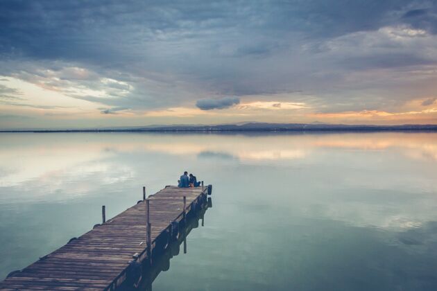 海美丽的情侣坐在美丽的夕阳下的木码头上海滩云浪漫
