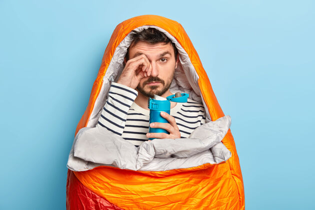 假期疲劳不刮胡子的男性揉眼睛 有睡意 野营旅游 在睡袋里放松 享受冒险周末站徒步旅行冒险