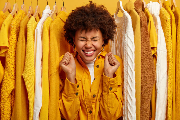 Positive人们 穿衣 购物的概念快乐的黑皮肤女人带着牙齿微笑 握紧拳头 站在衣柜之间的衣服壁橱FemaleSale