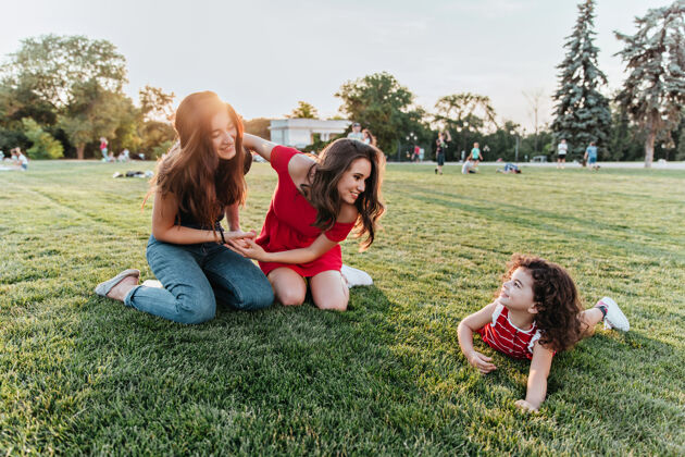 黑发漂亮的女性朋友和小孩在草地上合影漂亮的卷发女孩和姐妹们在公园里共度时光游戏童年公园