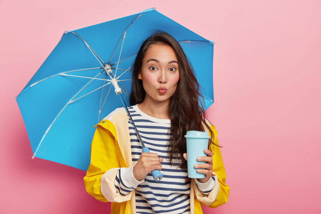民族美丽的亚洲年轻女性在雨天上大学 用雨伞和雨衣保护自己天气季节散步