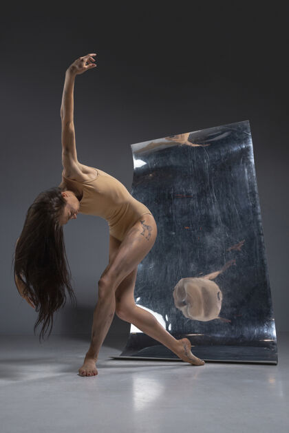 现代年轻时尚的现代芭蕾舞演员 在灰色的墙壁上 镜子和幻觉反射在表面上柔韧性和运动的魔力创意艺术舞蹈的概念 动作和灵感点长度对比
