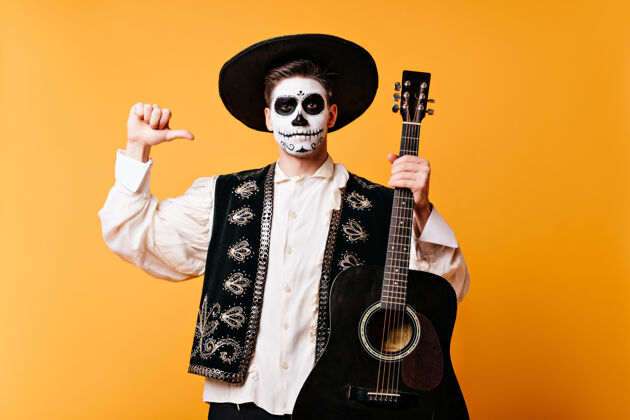 室内戴帽子的墨西哥人用手指着吉他隔着一堵墙 一个穿着传统服装 脸上画着艺术的家伙的快照西班牙语男模角色