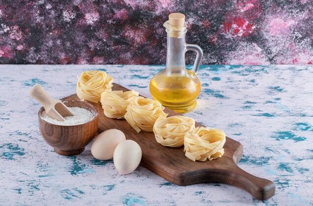 生的意大利面用面粉 鸡蛋和橄榄油在木板上筑巢面食食物瓶子