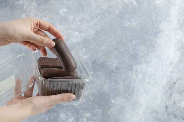 糖女人手里拿着一个塑料盒子 盒子里的巧克力奶油卷被隔离在大理石背景上堆栈美食食物