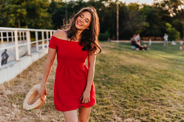 光一位手拿草帽的女士站在草地上一张身着红色连衣裙的时尚黑发女士在野外微笑的照片微笑户外幸福