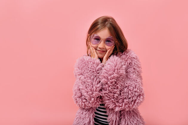 魅力快乐可爱的小女孩戴着圆眼镜和皮草时髦外套摆姿势太阳镜拥抱微笑