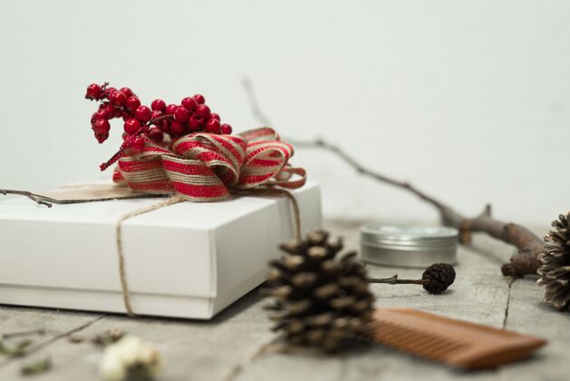 树枝一个白色圣诞礼盒的特写镜头 上面有一个红色的蝴蝶结 放在松果附近的桌子上设计概念灯