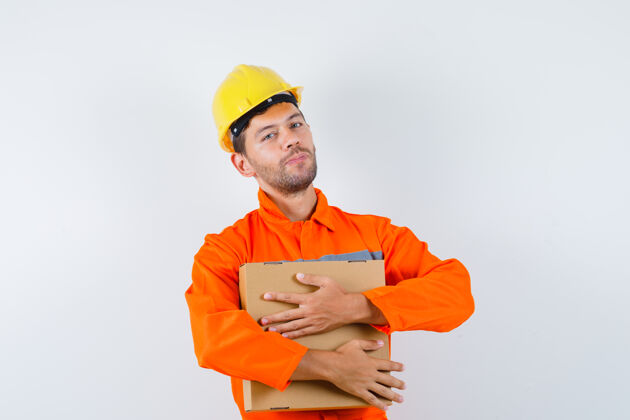 人穿着制服的建筑工人 戴着头盔拿着纸板箱 看上去很正面 正前方土建工程师职业