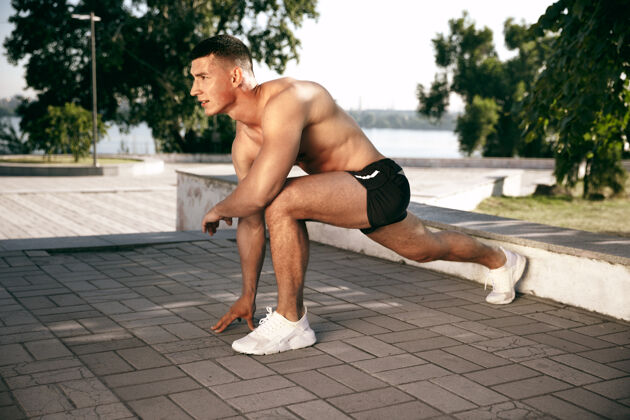 强壮一个肌肉发达的男运动员在公园里锻炼体操 训练 健身锻炼柔韧性夏日城市在阳光明媚的日子里在太空场上动作力量健美