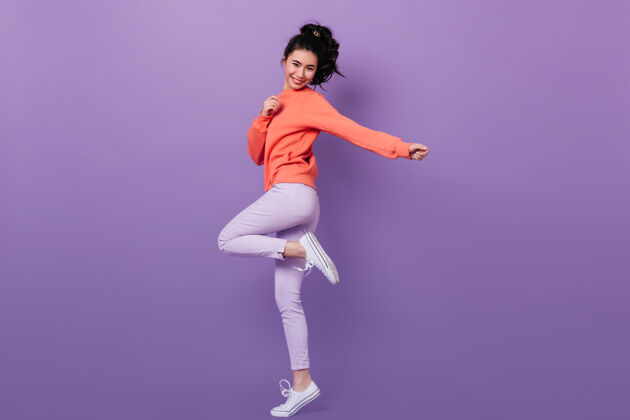 人快乐的中国女孩单腿站立的全景无忧无虑的亚洲女模特在紫色背景下跳舞的摄影棚镜头美丽有趣庆祝