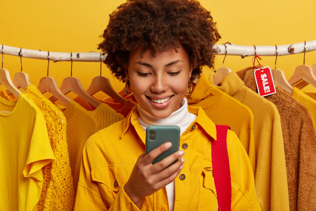 标签很高兴网上商家专注于智能手机设备 站在黄色衣服的货架上零售卷发女士