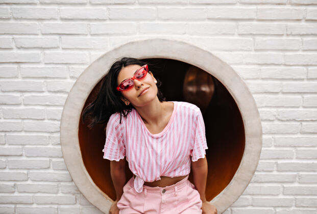 享受穿着t恤的快乐女人坐在砖墙上戴着时髦太阳镜的迷人女人的户外照片现代复制空间装束