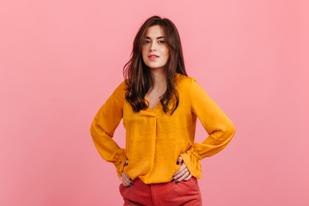 牛仔裤年轻漂亮的女模特 棕色的眼睛 穿着亮黄色的衬衫 在粉红色的墙上摆姿势年轻成人人