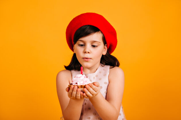 事件可爱的黑发小孩许生日愿望戴红色贝雷帽的少女吹灭蛋糕上的蜡烛寒冷蛋糕微笑