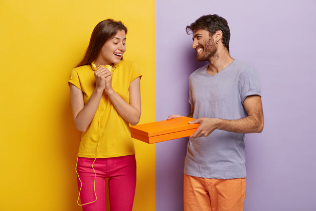 看友好的笑脸男给女朋友一个惊喜的纸箱 祝贺她胜利满意的黄t恤粉红裤女士很高兴收到好友的包裹站积极快乐