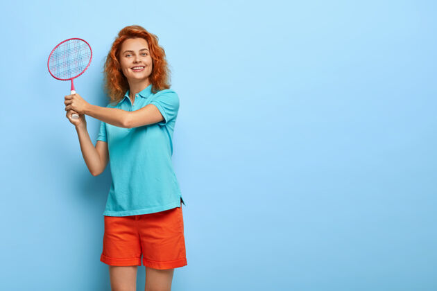 运动活泼的姜姑娘手拿网球拍 穿着休闲的蓝色t恤和红色短裤 和朋友一起享受游戏 有快乐的表情网球球拍高兴