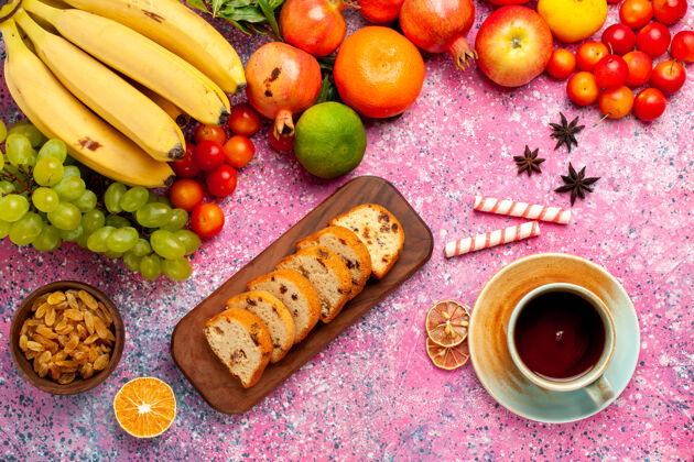 维生素俯瞰美味的水果组成与茶和切片蛋糕在粉红色的办公桌上香蕉美味成分