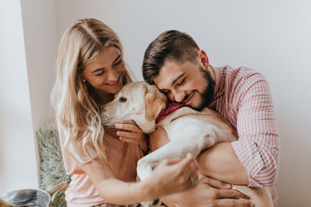 女朋友积极的夫妻玩狗穿条纹衬衫的男人温柔地拥抱拉布拉多微笑女性公寓