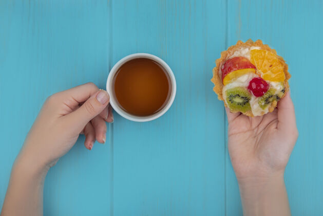 食物女性手拿水果馅饼和一杯茶的蓝色木制背景俯视图水果顶部木头