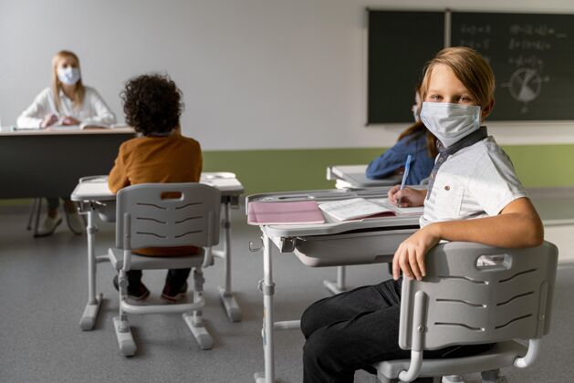 知识戴着医用口罩的孩子在学校和女老师一起学习课堂流行病新常态