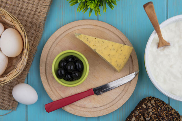 食物俯瞰奶酪与橄榄和刀架上的酸奶在一个碗在绿松石背景午餐乡村橄榄